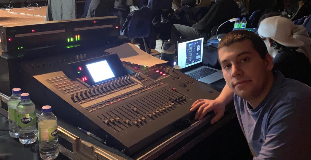 Tristan assis à la console de son, la salle de spectacle derrière lui.